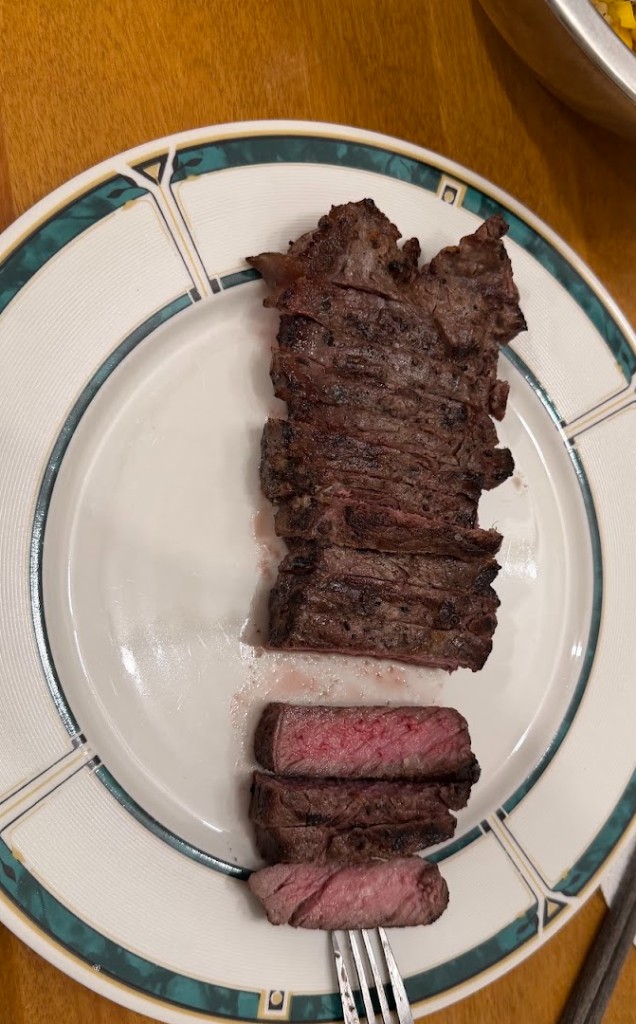 Sliced NY strip steak on a plate showing an even medium rare cook