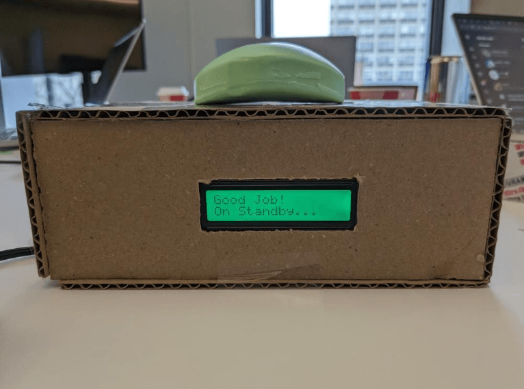 The finished soap alarm: a cardboard box with a bar of green soap on top and an LCD on the front reading 'Good Job! On Standby...'