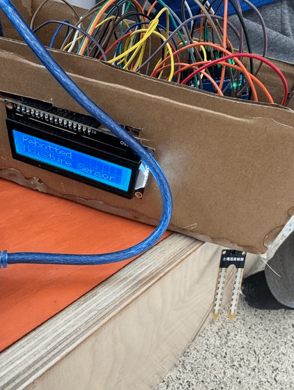 The soil moisture sensor build: an LCD reading 'Repotted Moisture Sensor' mounted on a cardboard box, with a soil moisture probe beside it