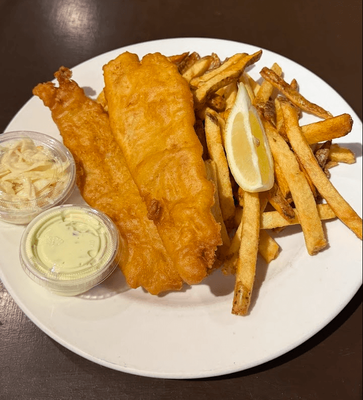 Fish and chips from Fresco's: two pieces of battered cod, fries, a lemon wedge, coleslaw, and tartar sauce on a white plate