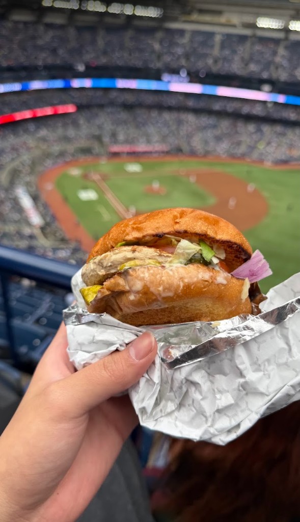 Grilled chicken sandwich from South St Burger held up in front of the baseball field at a Blue Jays game
